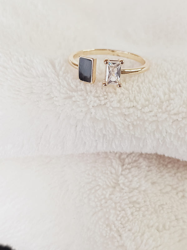 Gold ring with a black gemstone and clear stone on a textured white surface
