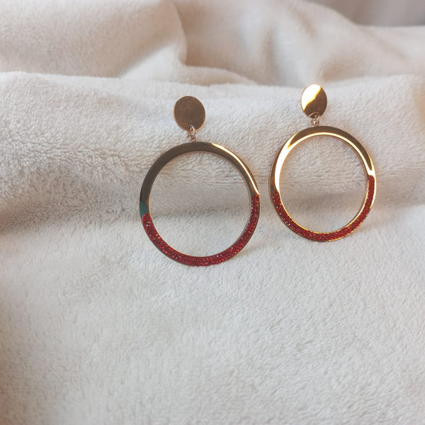 Gold hoop earrings with red interior on a white fabric background